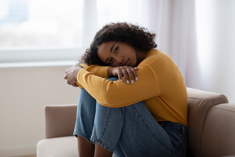 Young depressed black women having mental disorder hugging her knees on sofa at home